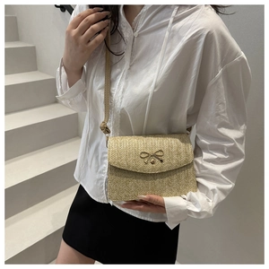 Detailed straw texture and metal bow decoration on a woven beige crossbody bag