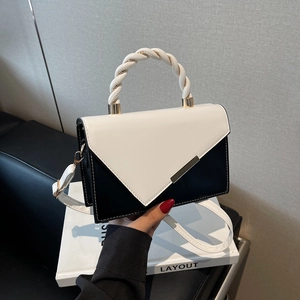 Sac bandoulière bicolore avec poignée tressée posé sur un magazine de mode