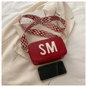 Détail du sac photo carré rouge avec lettres SM et bandoulière large en tissu à motifs