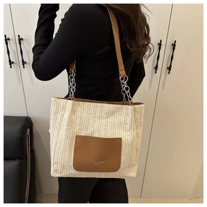 Dettaglio della borsa tote in paglia intrecciata con tasca in pelle marrone e catena