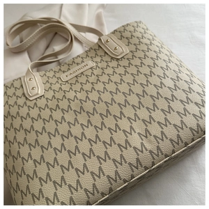 Close-up of beige tote bag with M-pattern print, fashion label and golden rivets