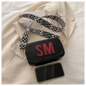 Détail du sac bandoulière noir avec patch SM rouge et bandoulière tissée large