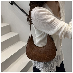 Brown woven crescent hobo bag shown on model's shoulder against a white spiral staircase