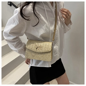 Close-up of woven straw crossbody bag with golden bow clasp and thin leather strap