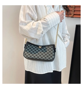 Detail of a chic black shoulder bag with grey M-letter prints and gold chain strap