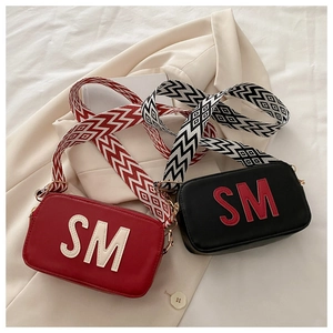 Détail de sacs bandoulière rouge et noir avec écussons SM et larges sangles à motifs