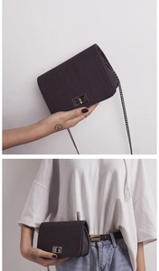 Detail view of a compact black crossbody bag with metal chain strap and twist lock clasp