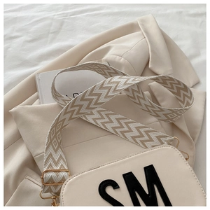 Détail du sac bandoulière crème avec sangle géométrique large et écusson de lettre SM