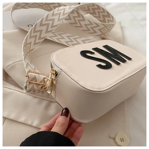 Détail d'un sac bandoulière beige avec sangle texturée et fermetures éclair dorées chic