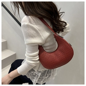 Side view of dark red croc-embossed crescent shoulder bag worn by model on stairs