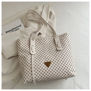Détail d'un sac cabas crème à motifs géométriques posé sur un blazer de couleur claire