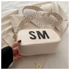 Détail du sac bandoulière beige avec patch lettre SM et sangle tissée large