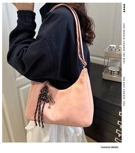 Close-up of pink suede shoulder bag featuring decorative tassel detail on a female model
