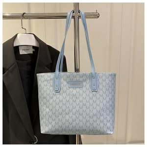 Close-up of light blue monogram tote bag with gold metal plaque and long shoulder straps