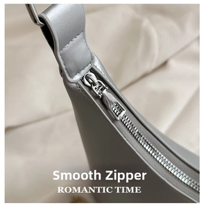 Close-up of smooth silver metal zipper and fine stitching on a grey leather tote bag