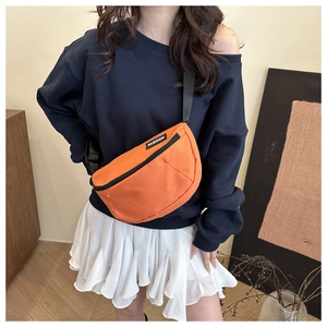 Detail of an orange canvas crossbody bag with black adjustable strap and fashion label