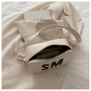 Détail du sac beige avec écusson SM et large bandoulière tissée géométrique