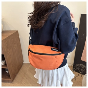 Detail of orange nylon saddle bag featuring fashion label and adjustable black strap