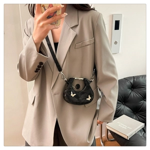 Détail du mini sac croissant en cuir verni noir avec papillons argentés sur costume gris