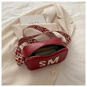 Détail du sac bandoulière rouge avec sangle large et dorures sur un blazer beige clair