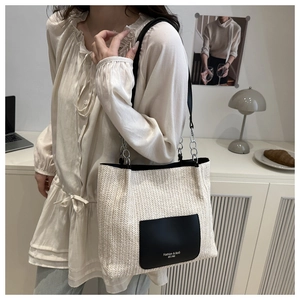 Detail of woven beige tote bag with black leather pocket and chain strap