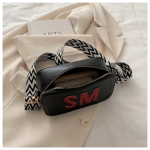 Détail du sac bandoulière noir avec écusson SM rouge et bandoulière à motifs géométriques