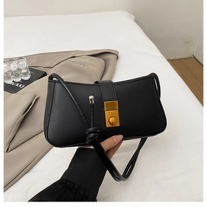 Detail of black semi-circle leather bag featuring a gold rectangle buckle on white bedding