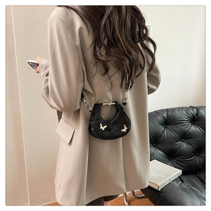 Détail d'un mini sac demi-lune noir avec papillons dorés porté sur un blazer de couleur kaki