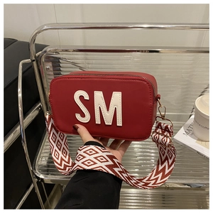 Détail du sac rouge avec broderie SM blanche et large bandoulière géométrique