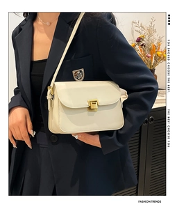 Détail d'un sac crème vintage avec fermoir doré porté sur un blazer bleu marine