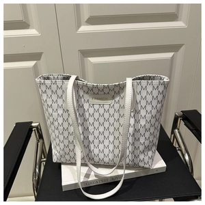 Detail of white tote bag with M-pattern and FASHION label on a minimalist chair