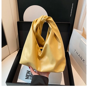 Detail of yellow pleated bucket bag with knotted handle in black gift box