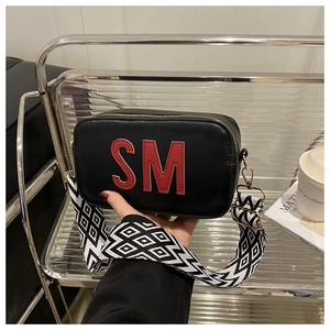 Détail du sac bandoulière noir avec broderie SM rouge et large sangle géométrique
