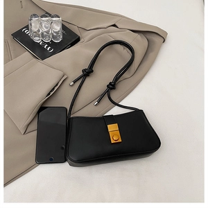 Detail of black matte leather baguette bag with gold rectangular clasp and knotted strap