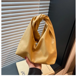 Detail of soft yellow faux leather handbag featuring a stylish knot handle design