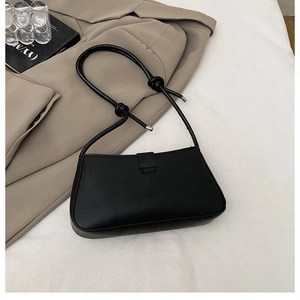 Detail of minimalist black leather baguette bag featuring unique knotted shoulder strap