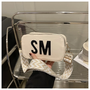 Gros plan du sac bandoulière crème avec lettre SM noire et large sangle tissée