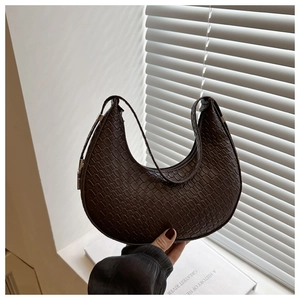 Macro shot of dark brown woven crescent bag with crocodile texture and silver metal buckle