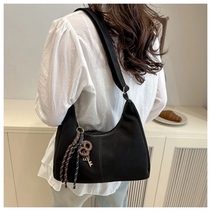 Detail of black crescent shoulder bag with woven pendant on model back in home setting
