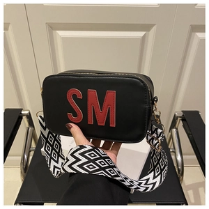 Détail du sac bandoulière noir avec patch SM rouge et sangle tissée géométrique