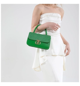 Detail view of the green glitter flap and gold circular twist lock on a leather handbag