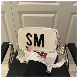 Détail du sac bandoulière crème avec écusson lettre SM et large bandoulière tissée