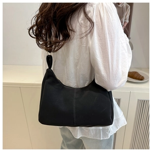 Side view of a minimalist black crescent shoulder bag worn by a model in a cozy room