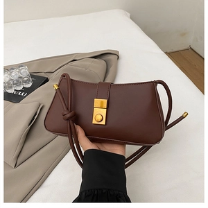 Detail of dark brown leather baguette bag featuring a gold square buckle and knotted strap