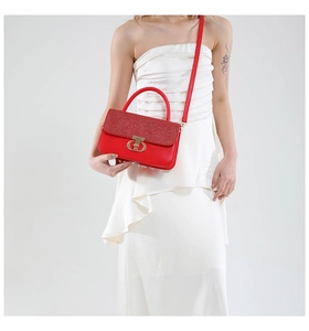 Close-up of elegant red leather handbag with sparkling glitter flap and gold metal T-lock