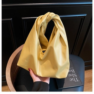 Detail einer leuchtend gelben Ledertasche mit einzigartigem Knotengriff und Faltenoptik