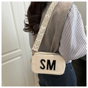 Détail du sac bandoulière crème avec logo SM et large sangle à motif géométrique