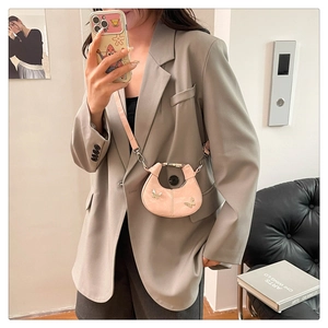 Gros plan du sac demi-lune rose avec détails papillons porté sur une veste grise