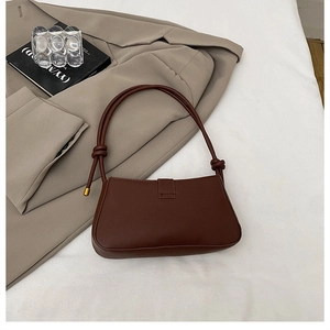Detail of a brown leather baguette bag with knotted strap on a clean white fabric background