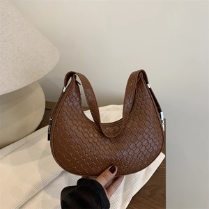 Brown woven pattern crescent hobo bag with adjustable silver buckle on a wooden desk